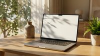 Modern laptop computer on wooden desk with plant shadows creating natural lighting atmosphere for remote work and productivity.
