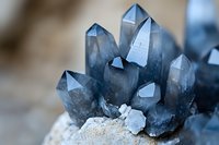 Blue smoky quartz crystal cluster formation with translucent pointed terminations emerging from rough stone base, macro mineral photography in soft light.
