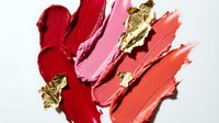 Luxurious lipstick smears in red pink coral shades with gold leaf accents on white background for cosmetic beauty makeup advertising campaigns.