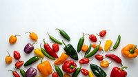 Assorted fresh peppers and chili peppers arranged on white background for cooking, recipe, and food styling projects.