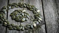 Green pumpkin seeds arranged in spiral pattern on rustic wooden background. Healthy snack, organic nutrition, superfood ingredient for cooking recipes.