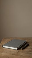 Closed hardcover notebooks with dark fabric covers stacked on wooden table against neutral beige wall, suitable for education, writing, and office design projects.