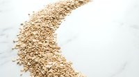 Scattered oat flakes forming curved path on white marble surface, representing healthy breakfast cereal, nutrition, and organic grain ingredients for food packaging and wellness content.