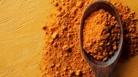Ground turmeric powder in wooden spoon on yellow background, aromatic Indian spice scattered around, macro food photography for cooking and wellness.