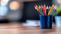 Colorful wooden pencils in blue ceramic holder against blurred office background with copy space. Creative workspace and art supplies setup.