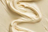 Creamy vanilla frosting swirls in smooth waves creating luxurious texture and pattern. Close up macro shot shows rich, glossy surface of white buttercream icing.