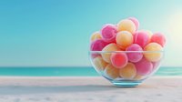 Colorful gummy candies in glass bowl on wooden table with tropical beach background. Sweet confectionery treats for summer vacation and holiday themes.