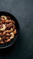 Mixed nuts in black bowl on dark slate background with copy space for healthy snacking and nutrition concepts.