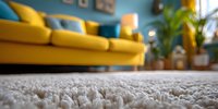 Close-up of soft white carpet in modern living room with bright yellow sofa, blue wall, and houseplants in background.