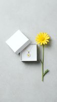 White jewelry gift box with daisy pendant necklace and fresh yellow flower on gray textured background for spring collection marketing and product photography.