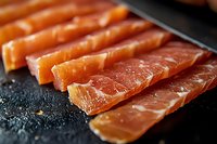 Fresh raw salmon fillet slices arranged in rows on dark surface, close-up view showing rich orange color and marbled texture of premium fish cuts.
