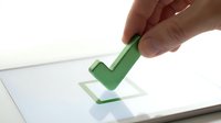 Hand holding green checkmark stamp over digital tablet screen showing completed task confirmation for business productivity and approval processes.