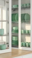 Organized white kitchen cabinet with mint green dishware, plates, bowls, and mugs neatly stacked on chrome wire shelves, bright interior.