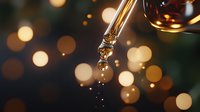 Macro shot of essential oil or serum droplet falling from glass dropper with golden bokeh lights in background creating luxurious spa atmosphere.