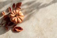 Small decorative pumpkin with autumn leaves on neutral beige background with soft shadows, creating minimal fall season composition.