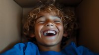 Mixed race child with curly hair wearing blue shirt laughing joyfully with eyes closed, showing genuine happiness and authentic emotion in natural lighting.