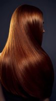 Woman with long glossy auburn hair shown from behind, rich copper tones gleaming against dark background, salon hair care concept.