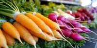 Fresh organic carrots and radishes with green tops displayed at farmers market produce stand for healthy eating and cooking.