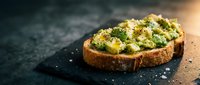 Avocado toast with herbs and seasoning on rustic bread slice, healthy breakfast or snack concept on dark slate surface.