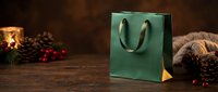 Green shopping bag with handles displayed on wooden surface surrounded by festive holiday decorations including pine cones, red berries, and warm lighting for seasonal retail and gift packaging.