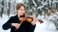 Young Caucasian male violinist performing classical music outdoors in snowy winter landscape wearing elegant black coat for concerts and recitals.