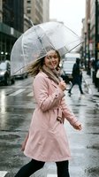 Young woman with long blonde hair, Caucasian ethnicity, wearing pink trench coat and black tights, holding transparent umbrella on rainy urban street with buildings.