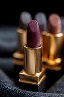 Luxurious purple lipstick in golden metallic case on dark background with soft focus. Close-up macro shot showcases rich texture and premium cosmetic packaging.