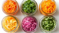 Fresh colorful fermented vegetables in glass jars from above. Homemade probiotics with carrot, cabbage, herbs arranged in rows on white background.