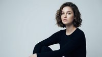 Young brunette woman in black sweater sitting confidently against gray background, professional portrait for business and lifestyle content.