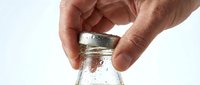Male hands opening a glass jar with white lid against neutral background, suitable for product packaging, food storage, and kitchen-related design projects.