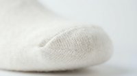 Close-up of a soft white knitted sock toe on a light background, showcasing texture and comfort for fashion or retail use.