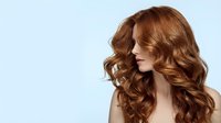 Young woman with luxurious curly auburn hair showcasing professional salon styling and healthy shine against clean background for beauty campaigns.