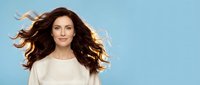 Young Caucasian woman with flowing brown hair in motion wearing white sweater against blue sky background for lifestyle and fashion concepts.