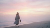 Woman with long hair in flowing dress walking alone on sandy beach at sunset with calm ocean and pink sky, suitable for wellness and lifestyle concepts.
