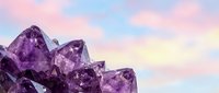 Purple amethyst crystals against dreamy pastel sky background for wellness, meditation and spiritual healing concepts.