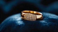 Elegant rose gold ring with pavé diamonds on rectangular surface against dark blue velvet background, luxury jewelry photography for engagement or wedding.