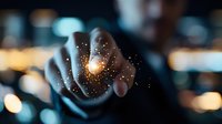 Magical glowing light particles floating between fingers against dark background with bokeh lights, creating mystical atmospheric effect.