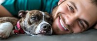 Happy young woman with brown hair lying close to her beloved senior pit bull terrier dog, showing the special bond between pet owner and loyal companion.
