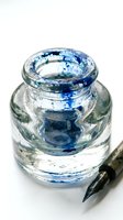 Glass jar filled with clear water and blue ink swirls, paintbrush with black handle nearby, isolated on white background for art and creative projects.