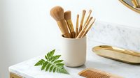 Natural bamboo kitchen utensils and wooden tools in ceramic holder with green fern leaf on marble counter for sustainable cooking and eco-friendly home decor.