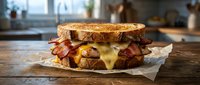 Grilled cheese sandwich with crispy bacon and melted cheese on toasted bread served on parchment paper in modern kitchen setting for comfort food concepts.