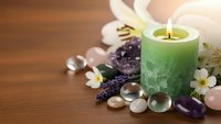 Green aromatherapy candle with healing crystals, white lily flowers and lavender sprigs on wooden surface for spa relaxation and wellness meditation.