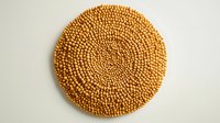 Golden wooden beads arranged in circular fibonacci spiral pattern on white background, natural material texture for design and decoration purposes.