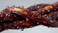 Glazed beef jerky strips with water droplets in macro photography showing texture and moisture on dark dried meat surface for food photography and advertising.