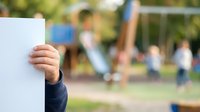 Child's hand holding blank white card with blurred playground background, suitable for advertising, marketing campaigns, educational materials, and promotional content.