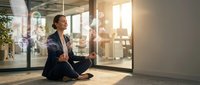Young professional woman meditating in modern office space during break time, practicing mindfulness and stress relief in corporate workplace environment.
