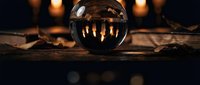 Crystal ball on wooden surface with warm candlelight reflections creating mystical fortune telling atmosphere for spiritual readings and divination practices.