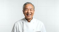 Senior Asian male chef wearing white chef's coat, smiling warmly at camera against neutral background. Professional culinary portrait for restaurant, cooking school, or food service industry use.