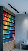 Modern home library interior with colorful books arranged by rainbow spectrum on wooden shelves with contemporary track lighting and minimalist design.