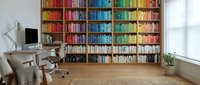 Modern home office with colorful organized bookshelf library wall, wooden desk, ergonomic chair and natural lighting for productivity and reading.
